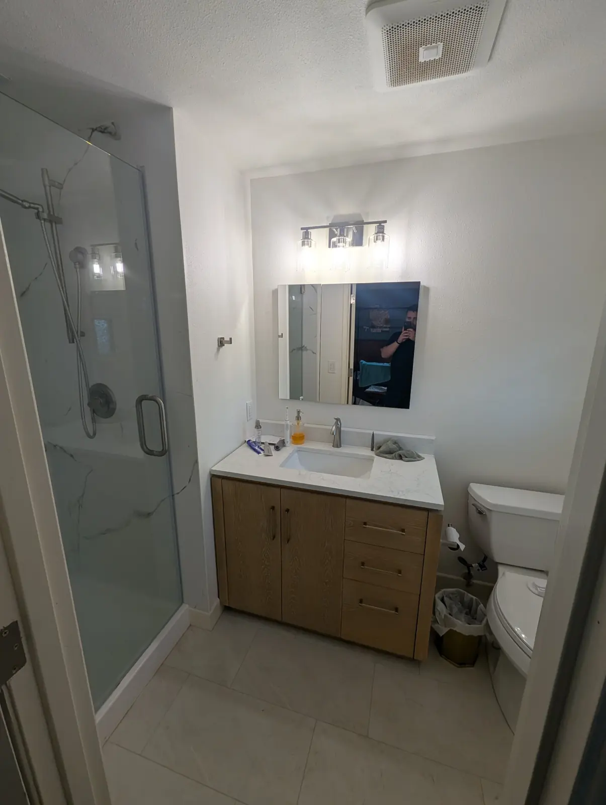 Finished bathroom with a glass shower door, marble-look shower walls, oak vanity and tile floor