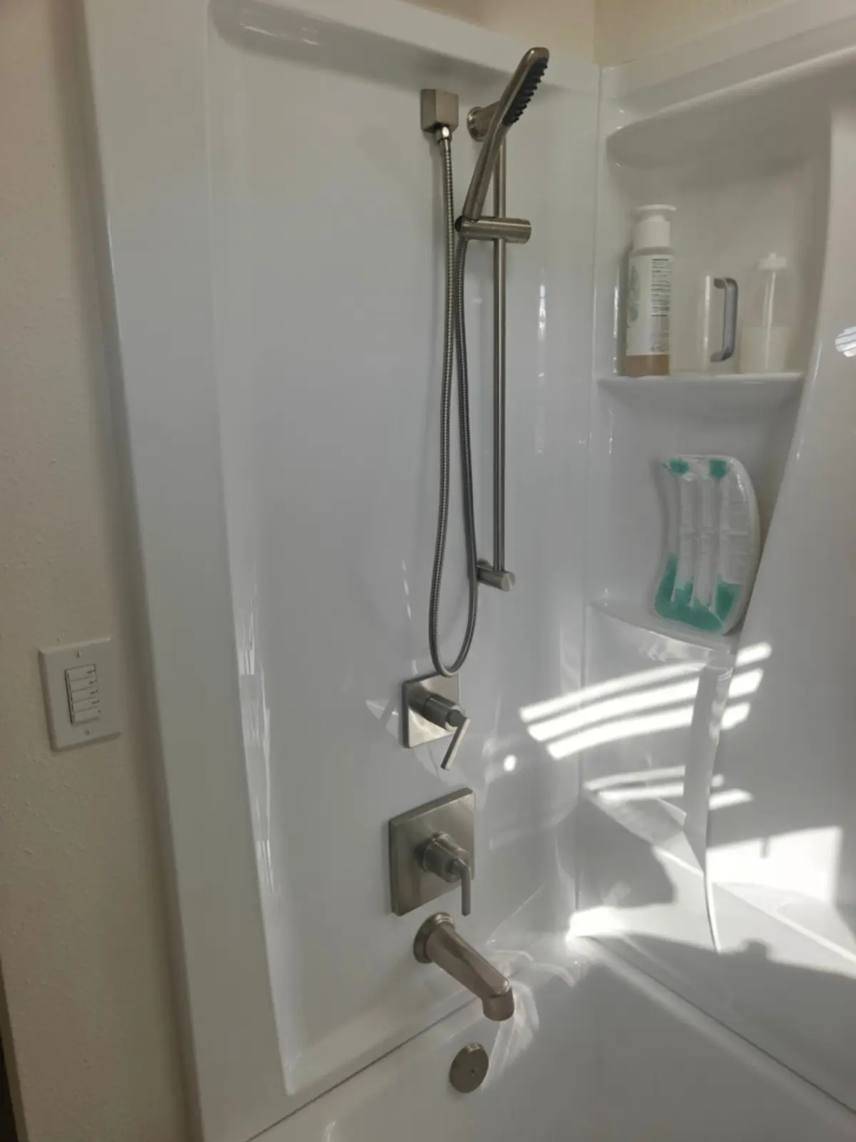 Tub surround with brushed nickel valve trim and a slide-bar handshower