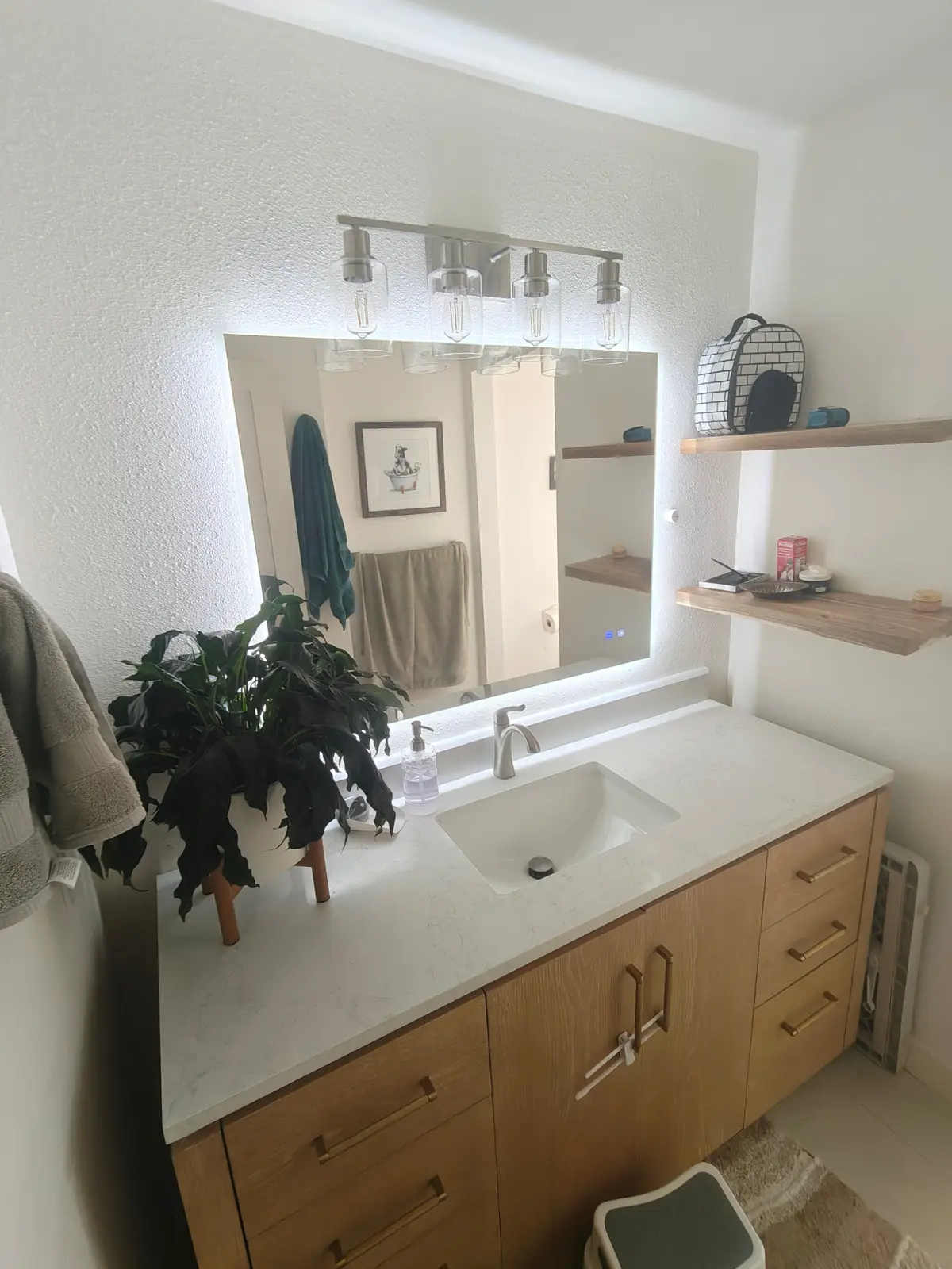 Remodeled bathroom with a white oak vanity, quartz top, backlit mirror and live-edge floating shelves