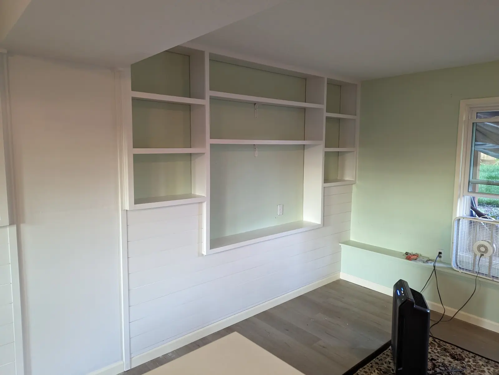 Finished white built-in shelving around a TV opening, with shiplap below