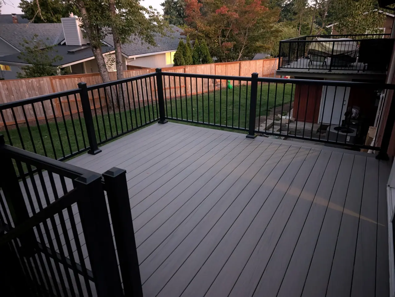 Gray composite deck with black aluminum railing overlooking a fenced backyard