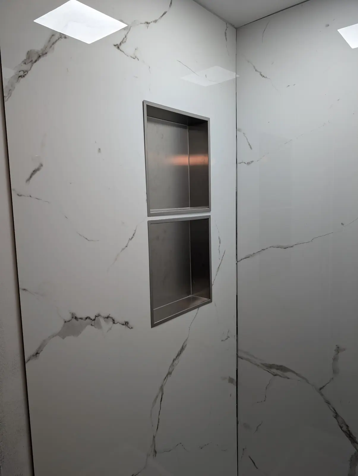Two recessed stainless steel niches set in marble-look shower wall panels